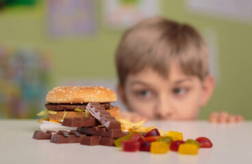 menino olhando na mesa hamburger, chocolate e jujubas